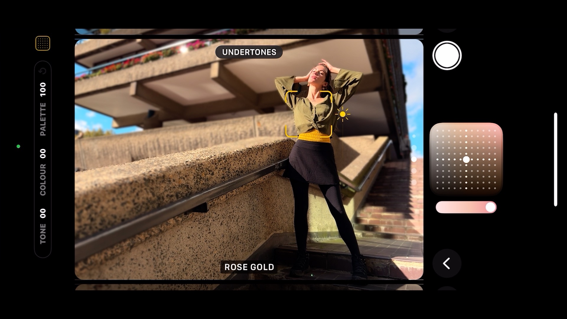 Screenshot of the camera UI from an Apple iPhone 16 Plus with a person having their portrait taken on a set of concrete steps