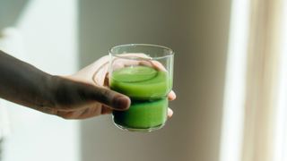 Woman's hand holding out a glass of green juice