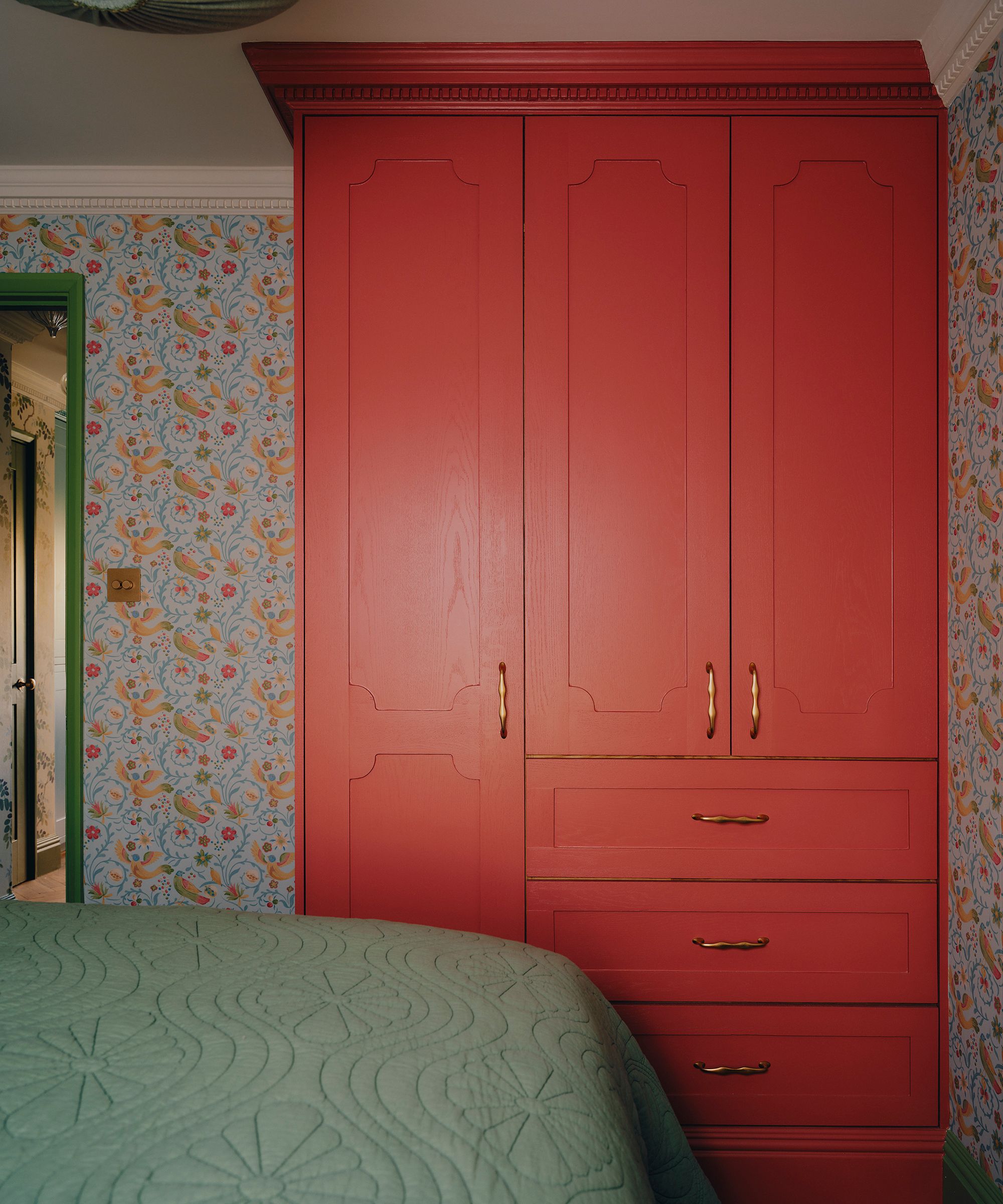 a floral wallpapered bedroom in London with traditional bespoke wardrobes painted red with Matilda Goad handles