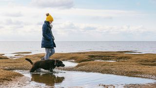 Woman walking a dog alone on the sea front, wearing yellow hat and coat