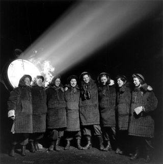 A line of women in clack suits and a window and light beam behind them