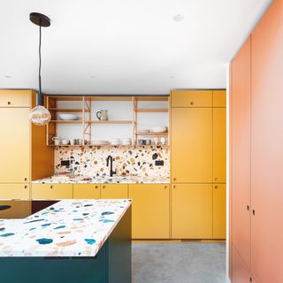 colourful kitchen with terrazzo island countertops, yellow cabinets, pink cupboard