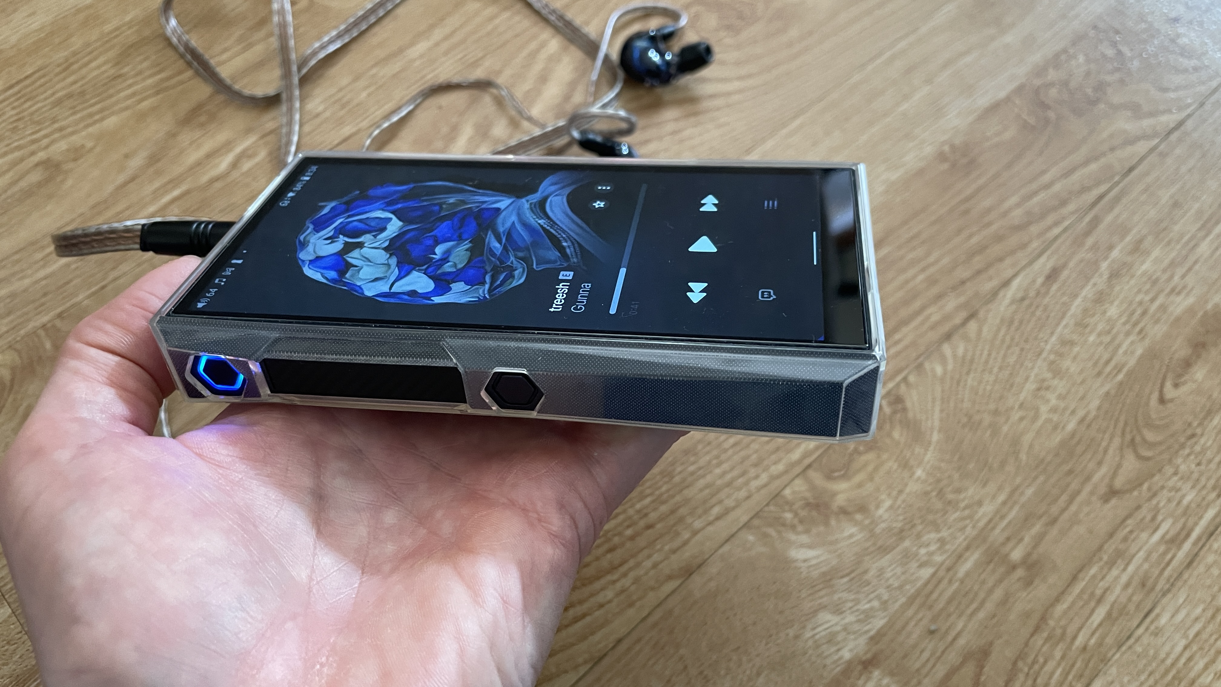 FiiO M23 player in a woman's hand, above a wooden table, playing Mogwai, Gunna and Fontaines DC