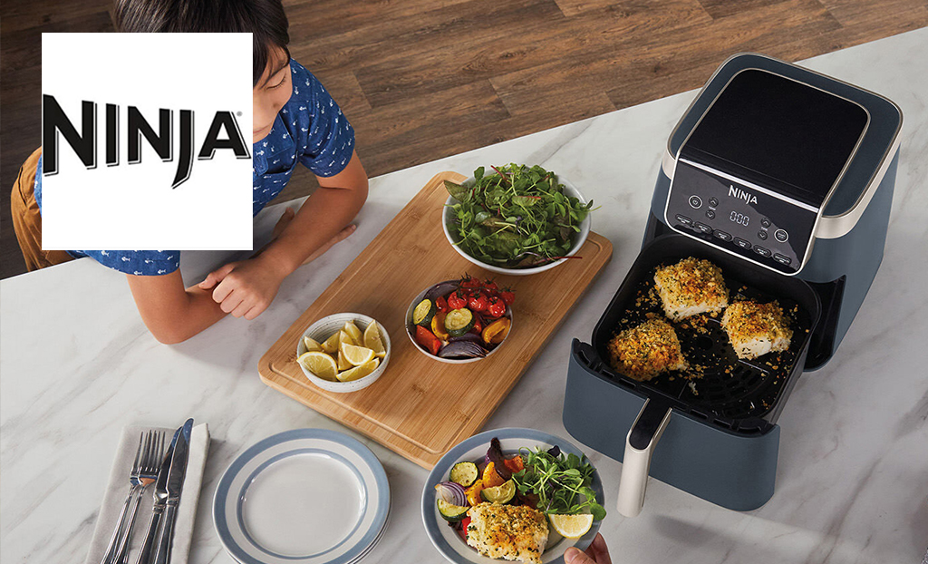 Ninja logo top left with a top down view of a ninja airfryer in use with a range of food on the table and a smiling child