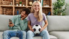 A woman smiles watching a soccer game, while a man next her sits looking bored on his phone