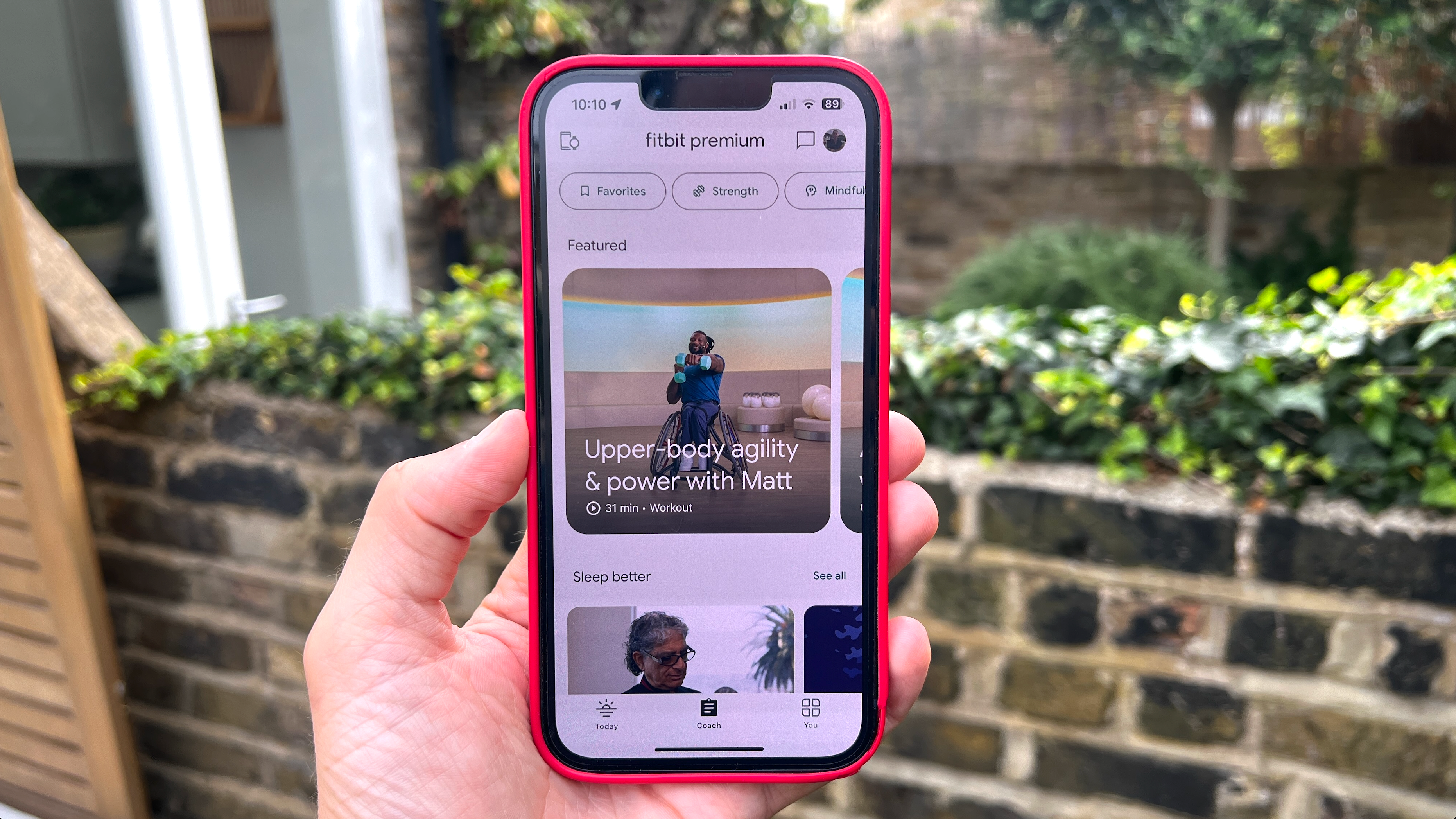Person holding an iPhone showing the Fitbit Premium section of the Fitbit app