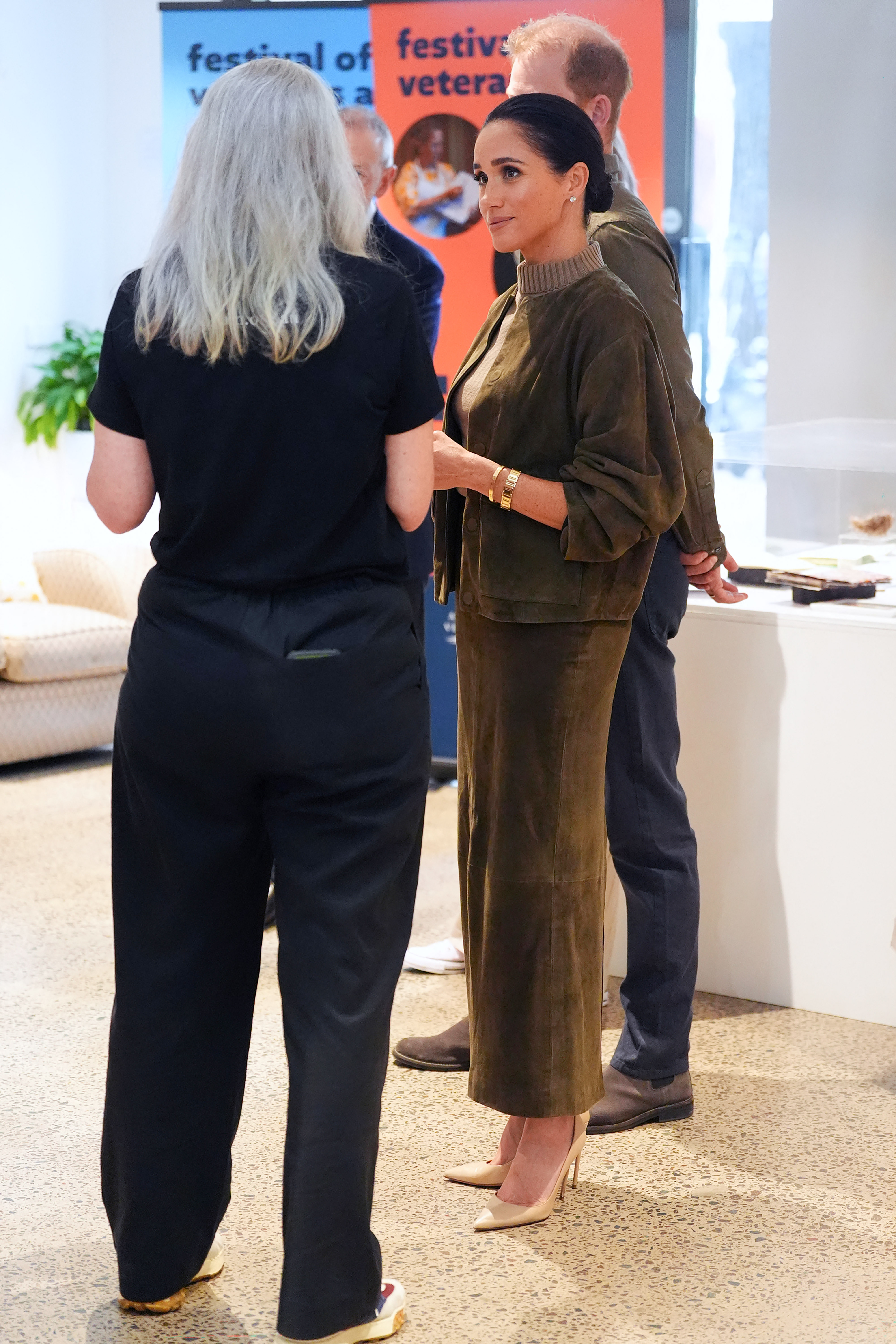 Meghan Markle wearing a green skirt and sleeveless top talking to people at a museum