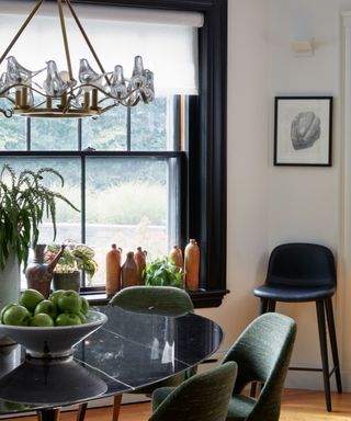 white dining room with black painted window frame, white blind, black stool, black table, olive chairs, antique chandelier, artwork, pots and vases