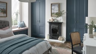 A blue bedroom with fitted shaker-style wardrobes, fireplace and window seat