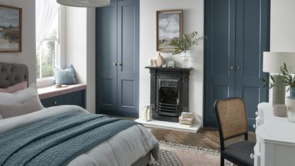 A blue bedroom with fitted shaker-style wardrobes, fireplace and window seat 