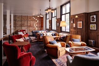 The hoxton lounge with red and mustard armchairs, wood paneled walls and Persian carpets