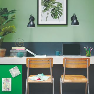 A home office desk with two chairs and a wall painted in green