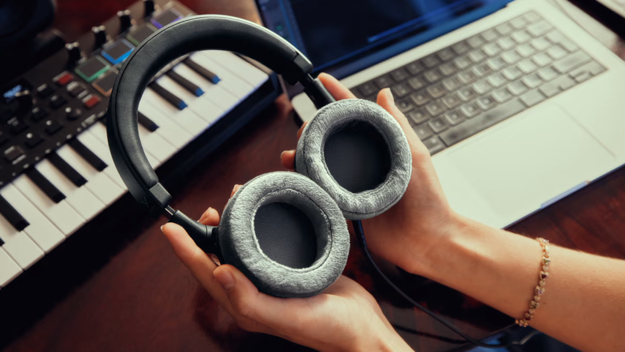 A pair of Beyerdynamic DT 270 Pro held to show their velour ear pads. A keyboard and Apple laptop are in the background