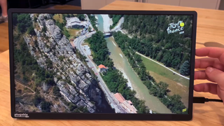 The Plugable Portable Display showing Tour de France highlights on a table with a hand next to the device.