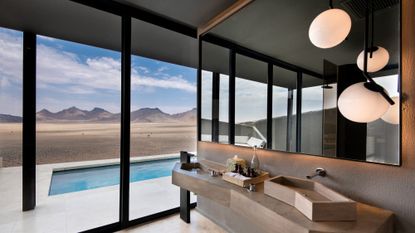 The sleek bathroom in a room at Sossusvlei Desert Lodge in Namibia with the desert and private pool seen outside the large windows