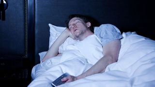 A man falls asleep in bed while watching TV