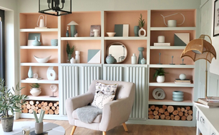 A living room with a built-in bookcase painted sage green with the alcoves behind a terracotta shade filled with ornaments and with an armchair placed in front