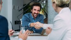 A financial adviser smiles and shakes hands with a new client.
