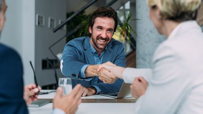 A financial adviser smiles and shakes hands with a new client.
