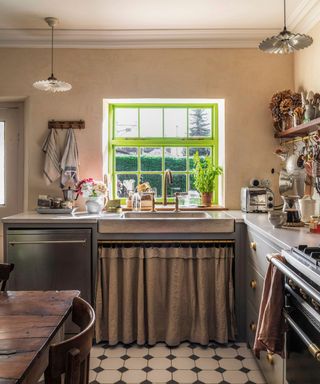 The sink in a French country style kitchen with a sink skirt and a green painted sash window frame