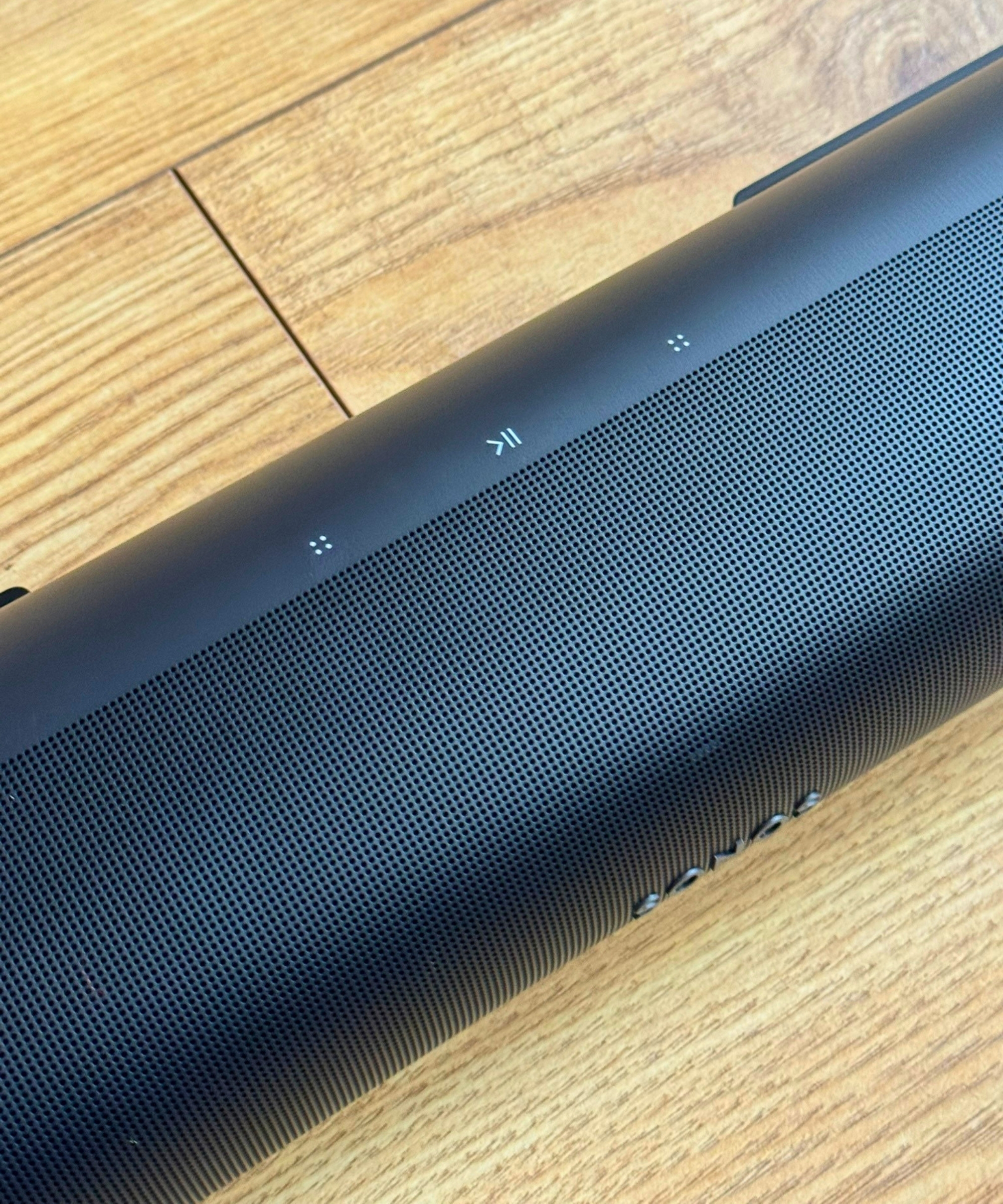Closeup of the Sonos Arc soundbar, showing three control buttons, on wooden floor.