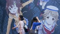 A late afternoon view shows two young women walking past a wall-sized anime mural along Chuo-dori (Central Avenue) in the Akihabara district (known as Electric Town for its maze of electronics stores, but currently considered an almost sacred destination by members of Japan's otaku culture, drawn to Akihabara's video game centers, maid cafes, anime shops, and manga comics), located in Chiyoda Ward in central Tokyo, Japan.