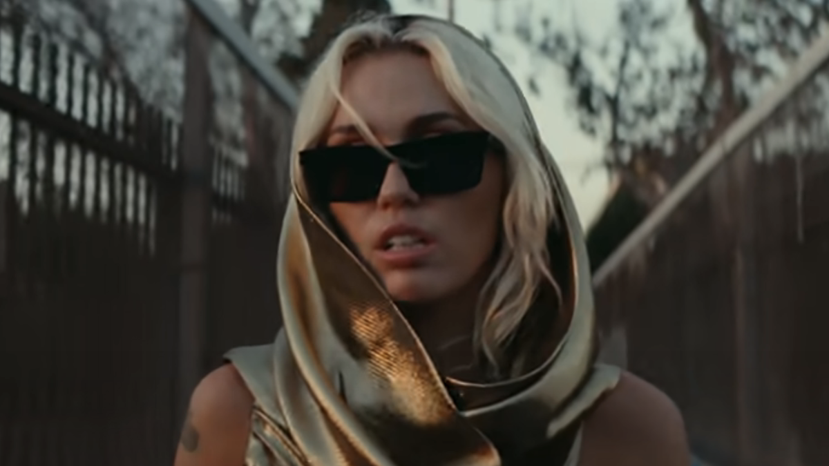 Miley Cyrus at the beginning of Flowers music video, wrapped in a gold head wrap sunglasses.