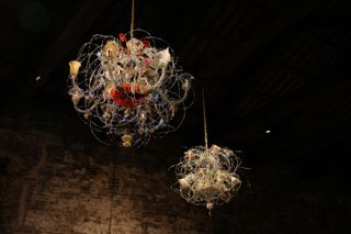 Two Murano glass chandeliers hang in a darkly lit brick building.