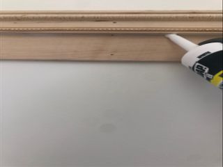 DIY board and batten tutorial with person caulking wooden trim on white wall