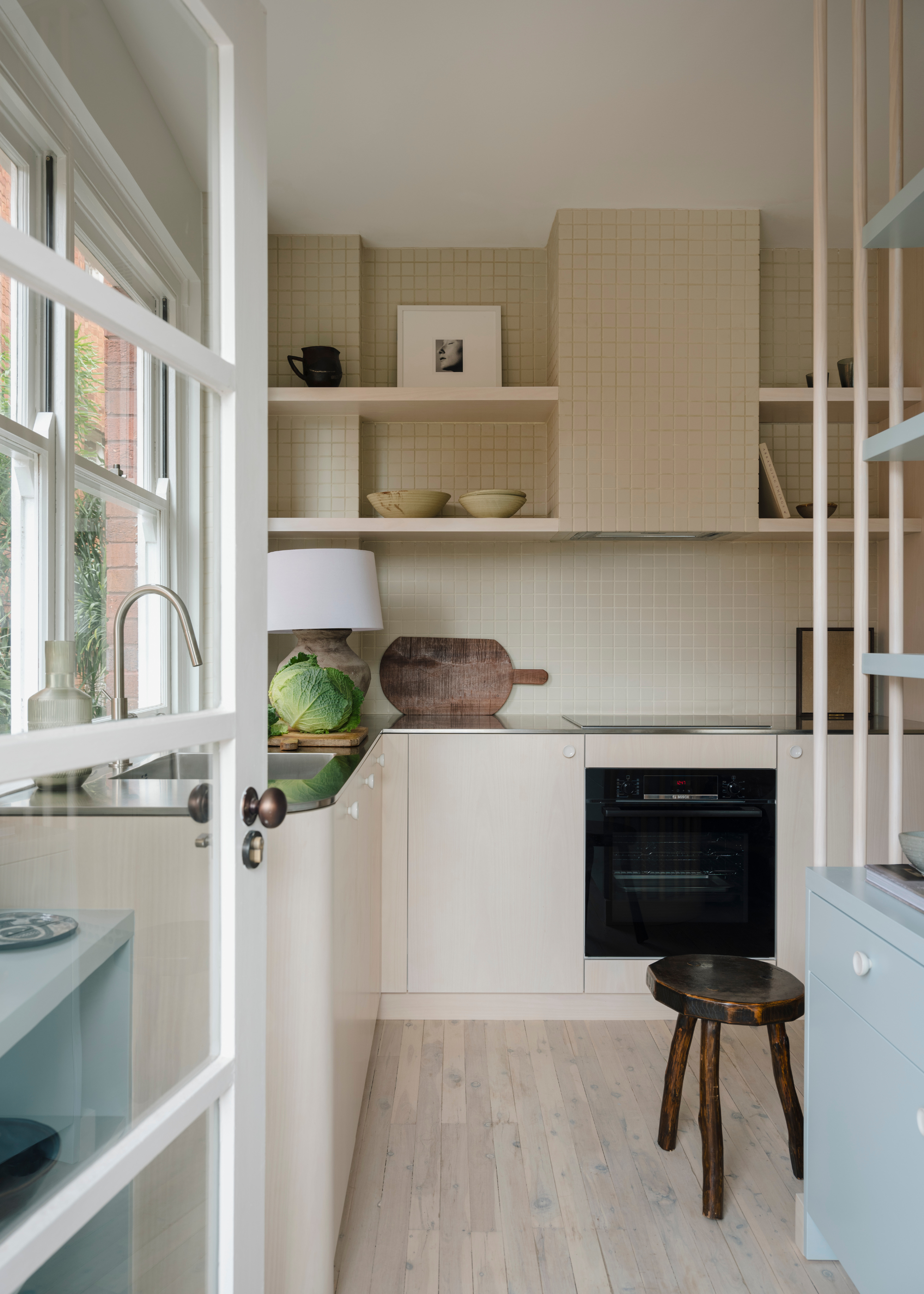 A small kitchen with a tiled backsplash, a head of lettuce on a chopping board and in-built shelving