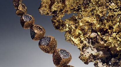 A close-up of seven connected gold / diamond stones adjacent to a large gold-coloured leaf object. 
