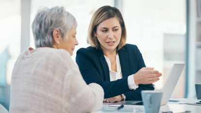 A financial adviser shows a client something on her laptop in her office.