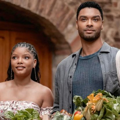 halle bailey and rege jean page smiling on a balcony with produce in front of them in you me and tuscany