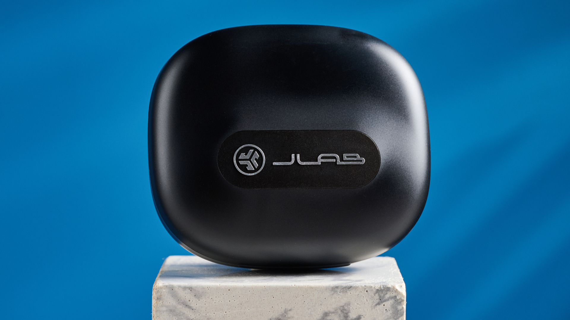 Jlab epic open sport open-earbuds in a black colorway photographed on a blue background.