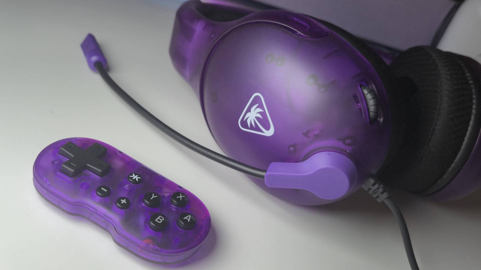 Photo of the CRKD Atom controller sitting next to the Ghost Purple Airlite Fit wired gaming headset.