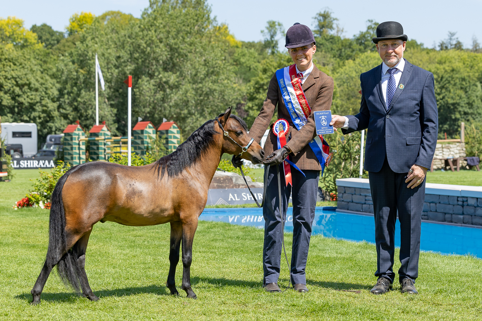 Miniature horse Maybe A Reign Star stands with handler Mia Hiscox who wears his championship sash and the judge for a photo at the 2026 Royal International Horse Show