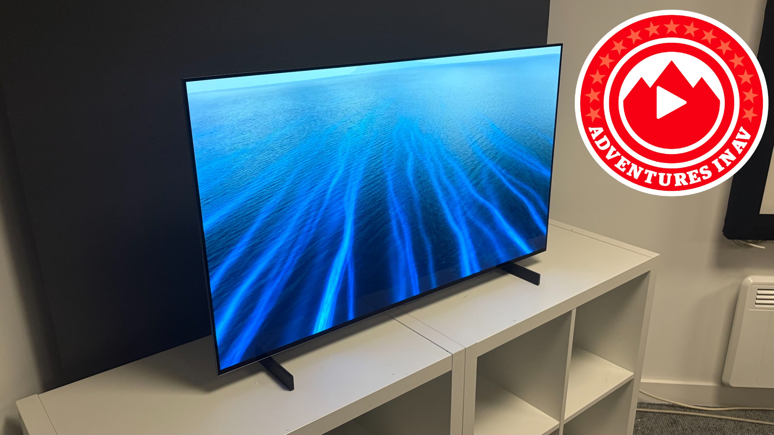 A 42-inch LG C6 OLED TV on a white set of shelves, with a logo next to it that reads "Adventures in AV2