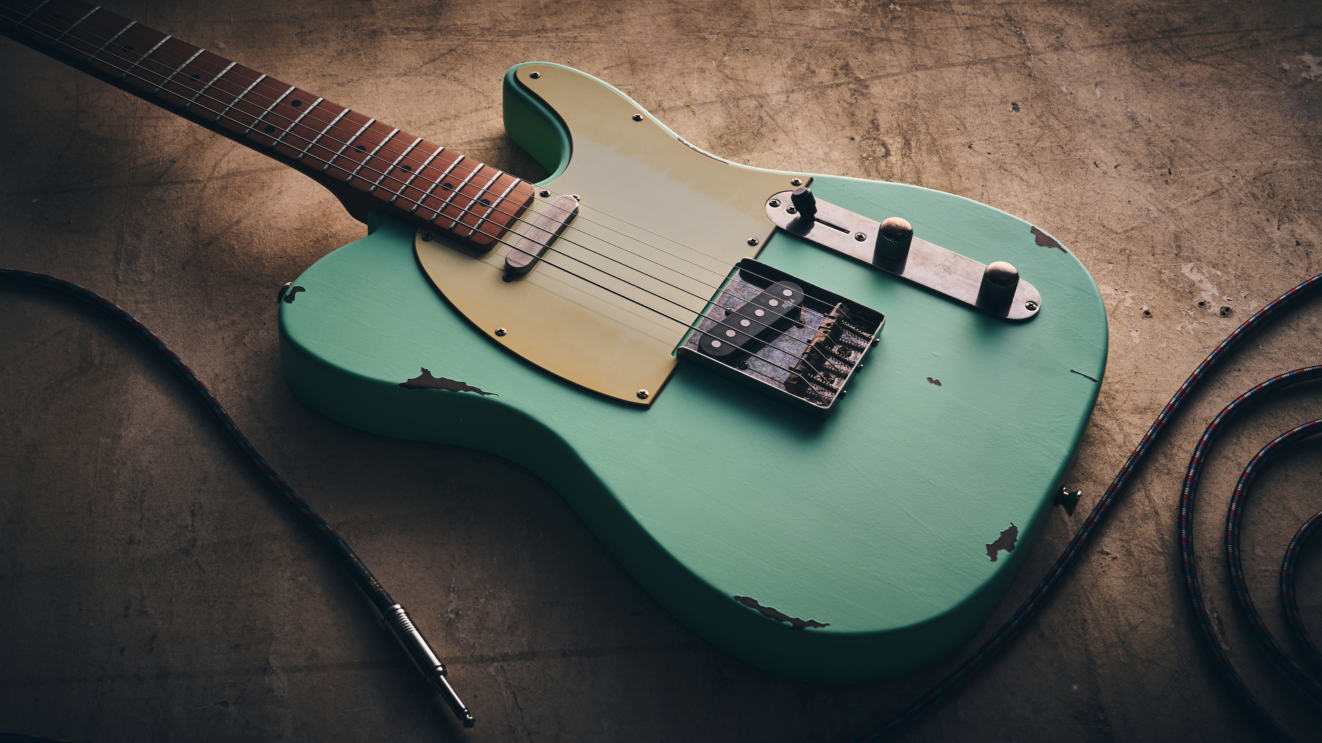A Harley Benton TE-62LA electric guitar on a distressed concrete floor with a guitar cable
