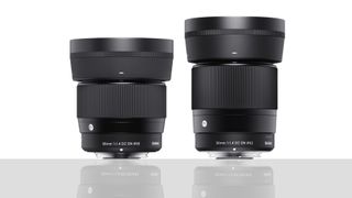 Sigma 30mm f/1.4 DC DN | C and Sigma 56mm f/1.4 DC DN | C lenses, against a white background, with reflections on a grey surface