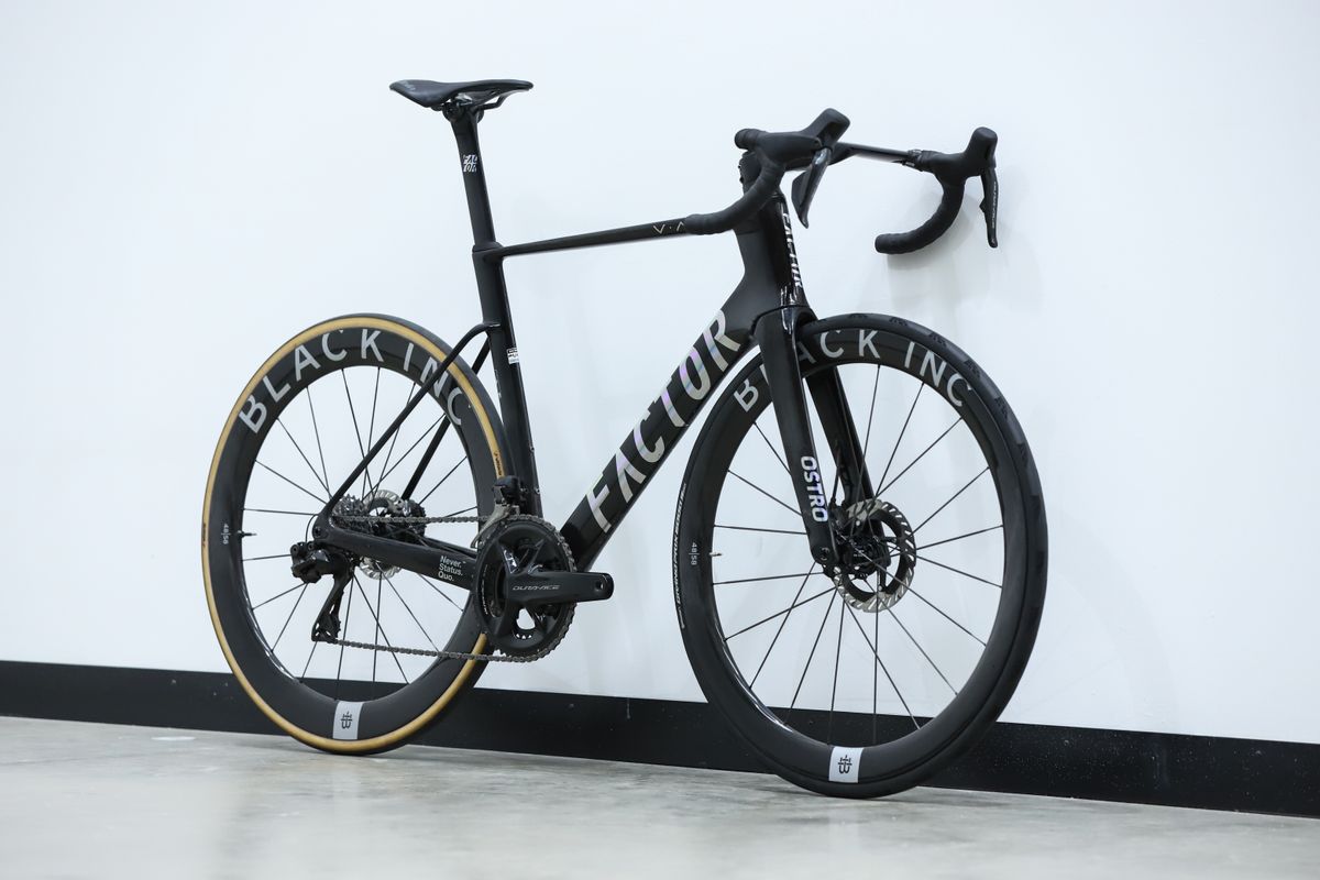 A Black Factor Ostro Vam leans against a white wall