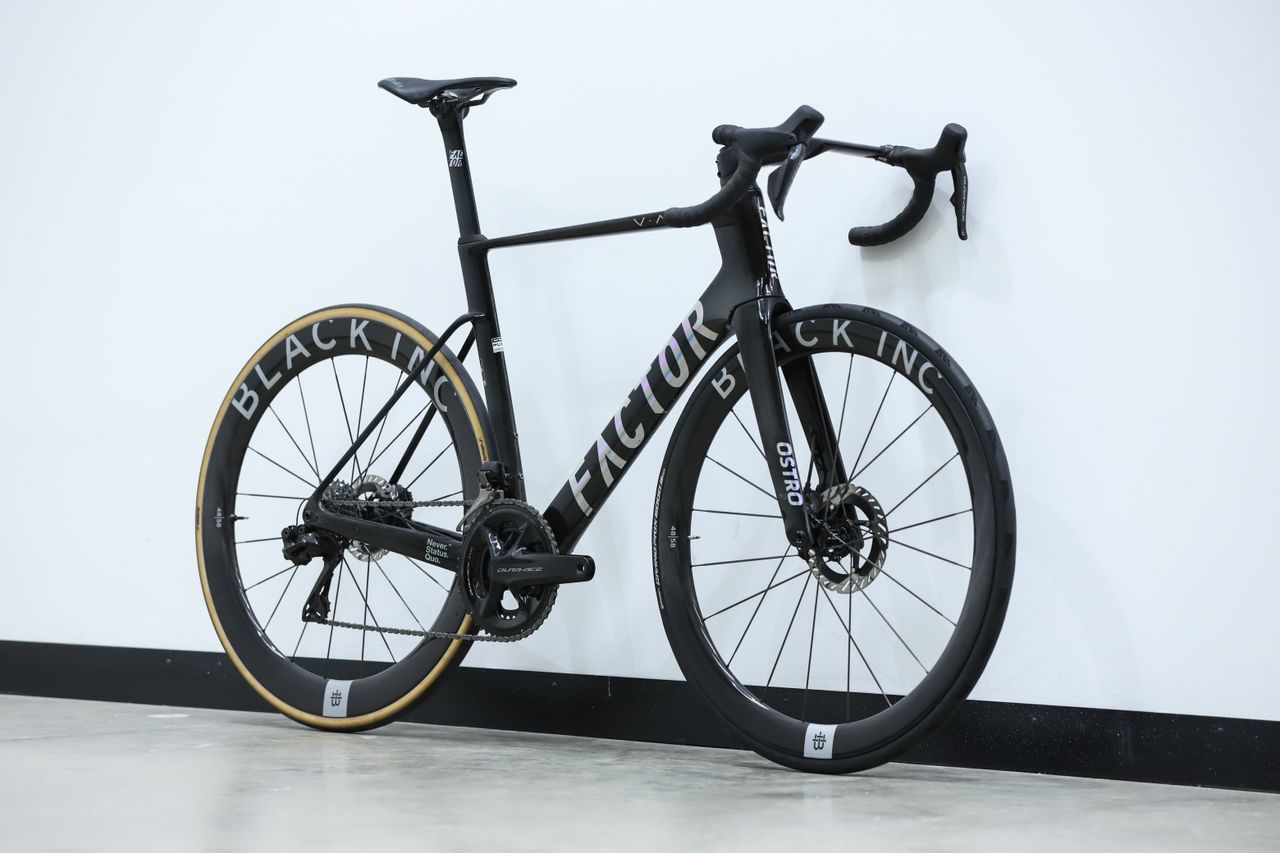 A Black Factor Ostro Vam leans against a white wall