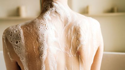 Best body wash for eczema - the back of a woman covered in shower gel lather - gettyimages 1447508636
