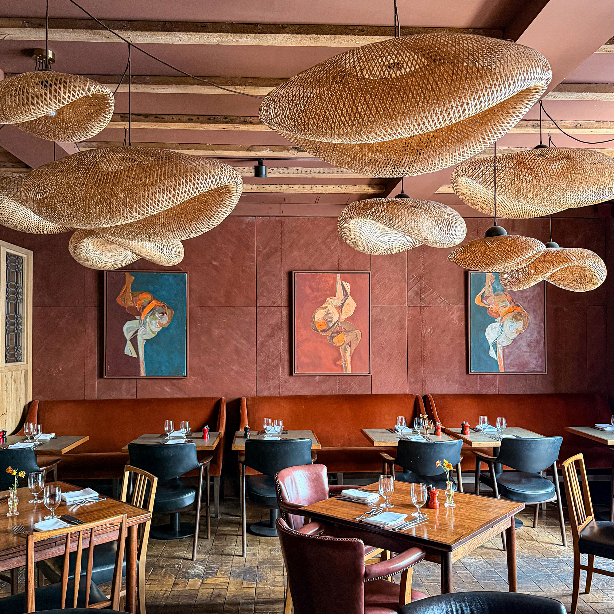 Hotel dining room with deep red walls, artwork, wooden ceiling beams and collection of oversized, sculptured woven ceiling light shades