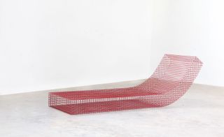 Red Modular lounge seating based on a grid structure, made of metallic net photographed in a room with white walls and grey floor.