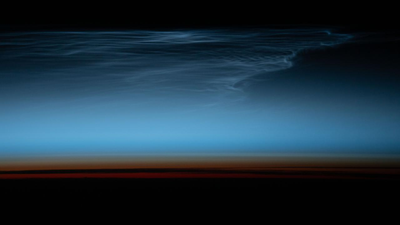 a dark, black hazy layer forms the base of this image of the sky, which creeps into a brief, dulled orange brown above the black, before an instant light blue, rolling up back into black as it rises. Blue wisps are illuminated from below as they blend with the rich, dark blue at the top.