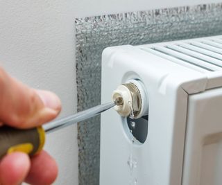 Someone turning a bleed valve on the end of a white, wall mounted radiator