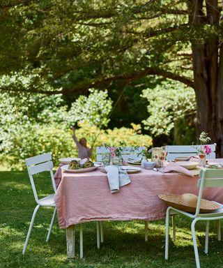 An example of outdoor garden ideas showing a white outdoor table with matching chairs and a pink table cloth