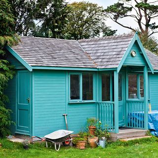 blue coloured garden shed with green lawn and potted plants