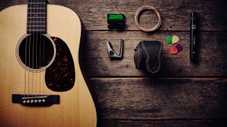 An acoustic guitar on a wooden floor with various accessories