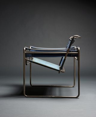 A textile and metal chair featuring dipped seat, photographed with a side view against a dark grey background